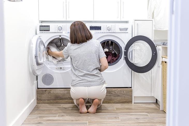 Mujer agachada frente a lavadora y secadora