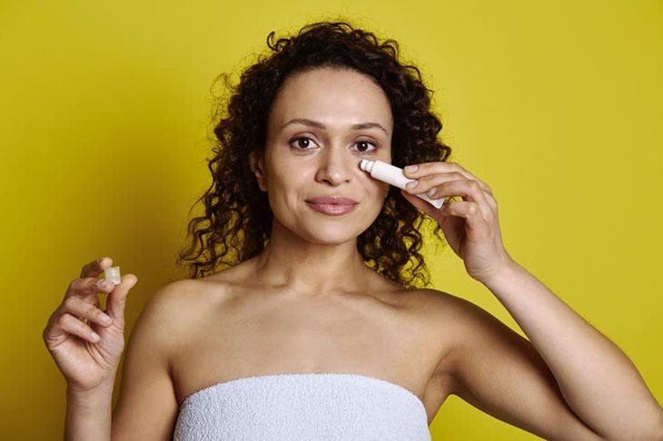Mujer usando un tubo de producto cosmético para el contorno de ojos