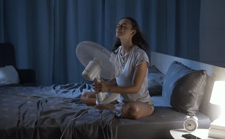 Femme utilisant un ventilateur pour supporter la chaleur de la chambre