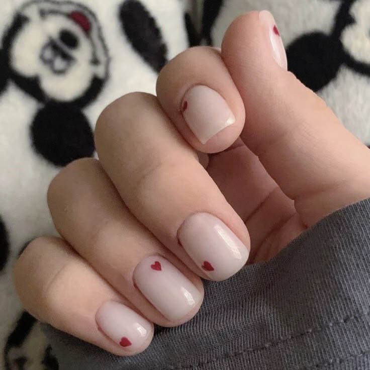 Ongles courts avec des motifs en forme de cœur rouge sur base nude Ongles courts avec des motifs en forme de cœur rouge sur base nude