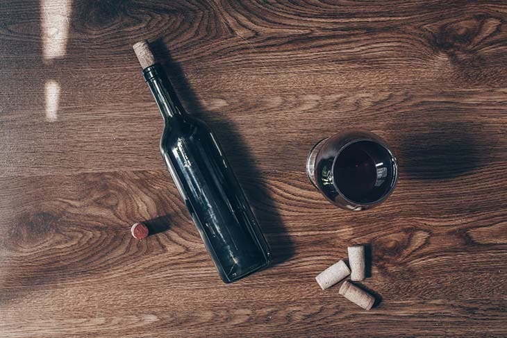 Une bouteille débouchonnée, un verre de vin rouge et des bouchons en liège sur une table en bois