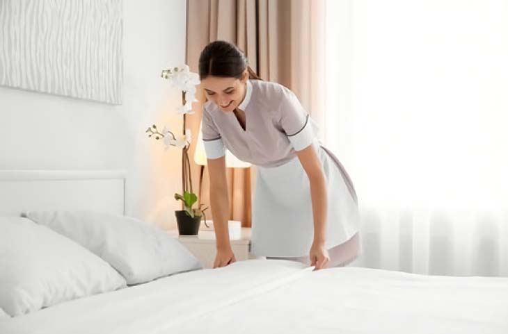 Une femme de chambre qui fait le lit d’une chambre d’hôtel