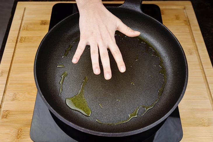 Una mano midiendo la temperatura de una sartén empapada en aceite de cocina